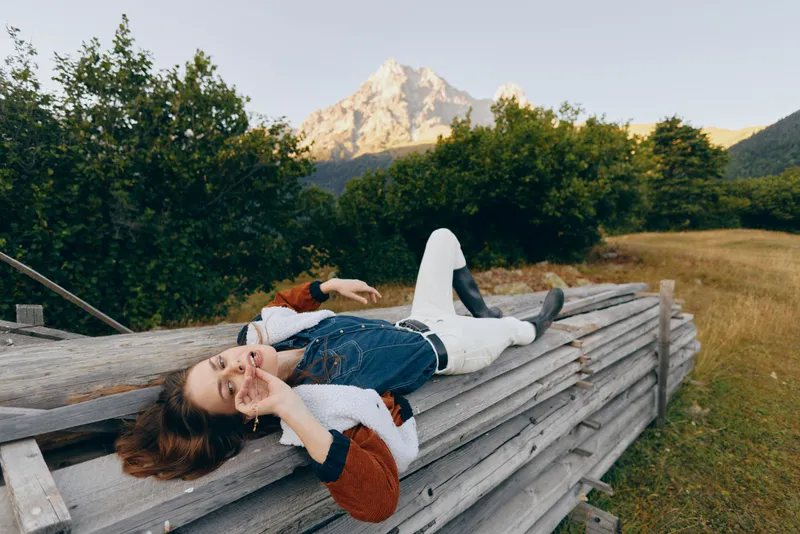 Woman relaxation on wooden fence in mountain meadow outdoors, portrait of casual young female lying back, enjoying nature, scenic landscape and peaceful summer escape.
