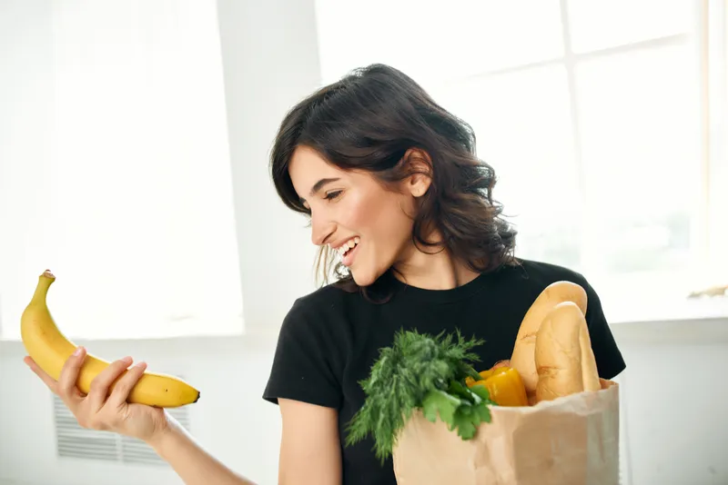 Жизнерадостная женщина с пакетом продуктов на кухне