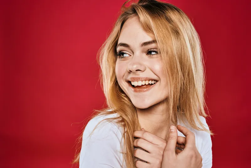Симпатичная женщина улыбается, на ней белая футболка, кадр обрезан ветвями на красном фоне