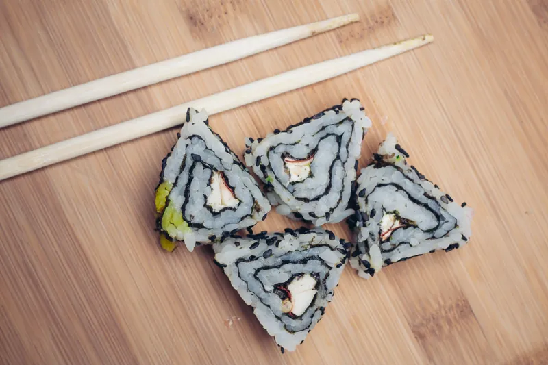 Треугольные роллы суши, палочки, деревянная доска, японская кухня