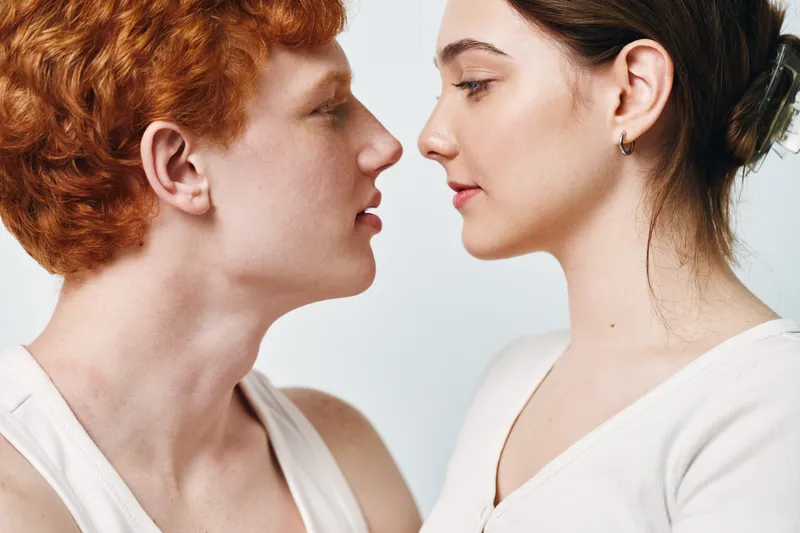 Teenage boy and girl face to face looking at each other closely with neutral expression on white background. Youth, young adult, intimacy and portrait of people closeup.