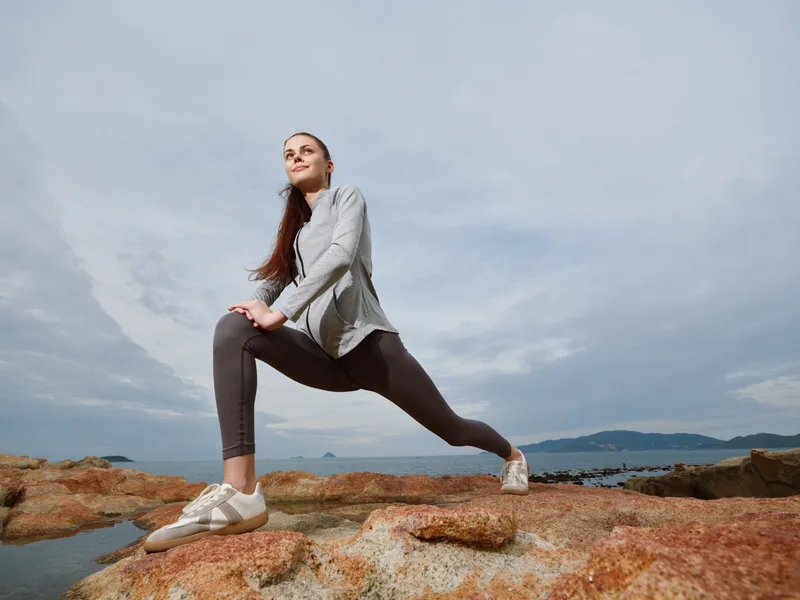 Young woman stretching on rocky beach during cloudy day, demonstrating fitness and healthy lifestyle with a focus on well being and motivation