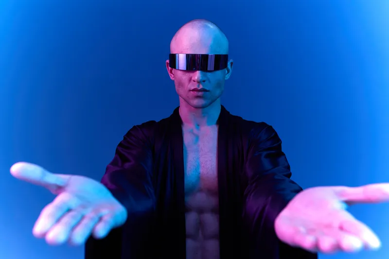 Futuristic man with a bald head wearing sunglasses extends his hands, showcasing a bold confident pose against a vibrant blue light background.