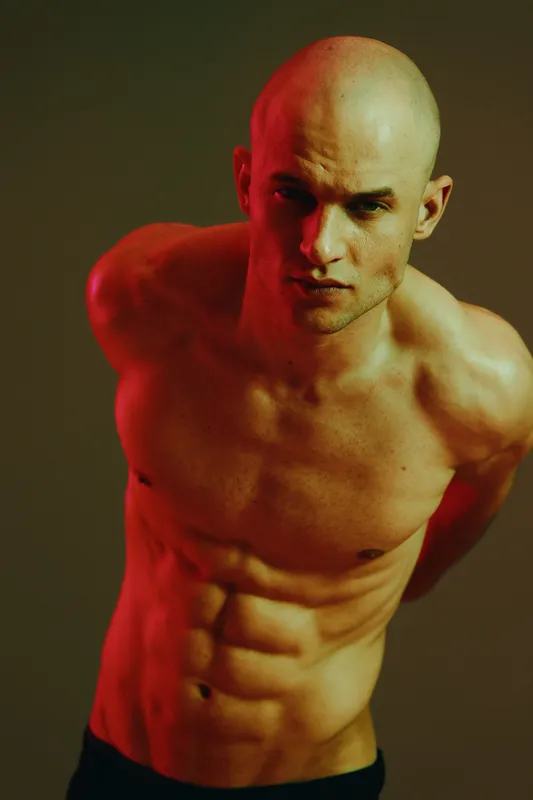 Strong man with an athletic build poses confidently, showcasing his toned physique against a dramatic background, illuminating the essence of strength and determination.