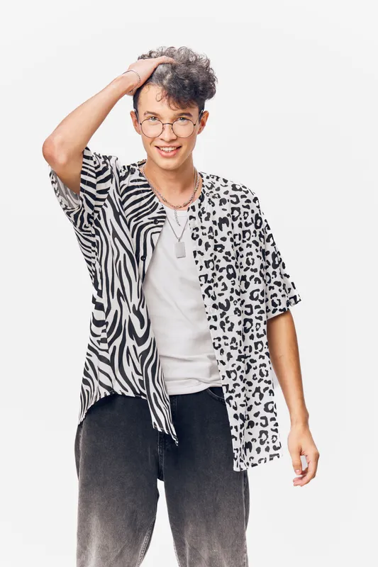 young man with glasses wearing a half zebra half leopard print shirt smiling confidently against white background in casual style with curly hair