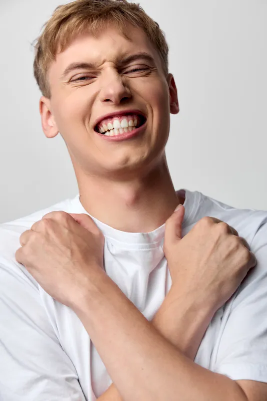 Energetic man in a white shirt grins broadly, arms crossed over his chest, exuding joy, confidence and self celebration with a bright mood, candid expression, and dynamic pose for lifestyle and