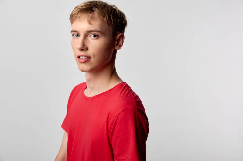 Young man in a red shirt posing in a studio, casual fashion and relaxed expression, clean background, suitable for lifestyle images and modern storytelling.
