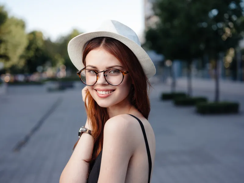 Счастливая женщина в белой шляпе и очках гуляет на природе по улице