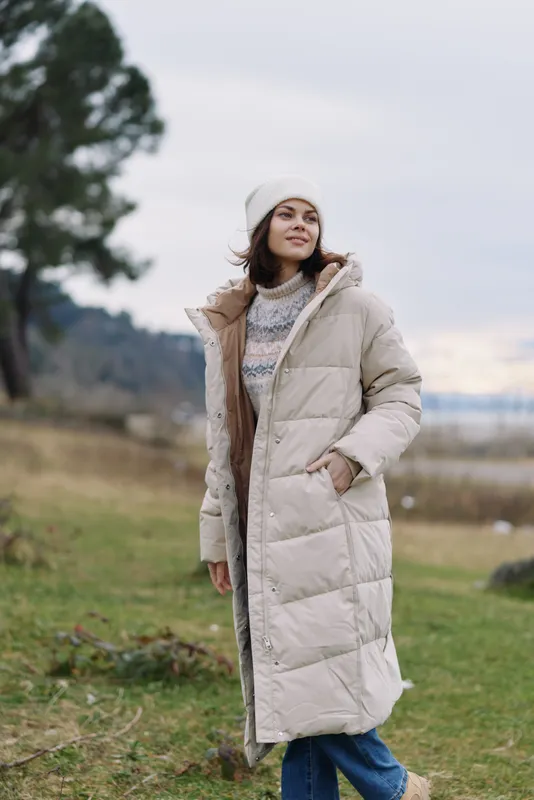 Winter coat on a woman standing outdoors in a cozy sweater, capturing casual fashion and lifestyle in a serene countryside setting, focusing on warmth and relaxed pose.