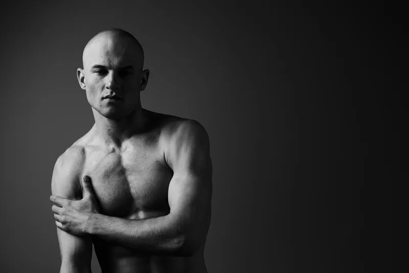Black and white portrait of a man with a serious expression, showcasing defined muscles and strong posture. This artistic image conveys emotion and strength effectively.