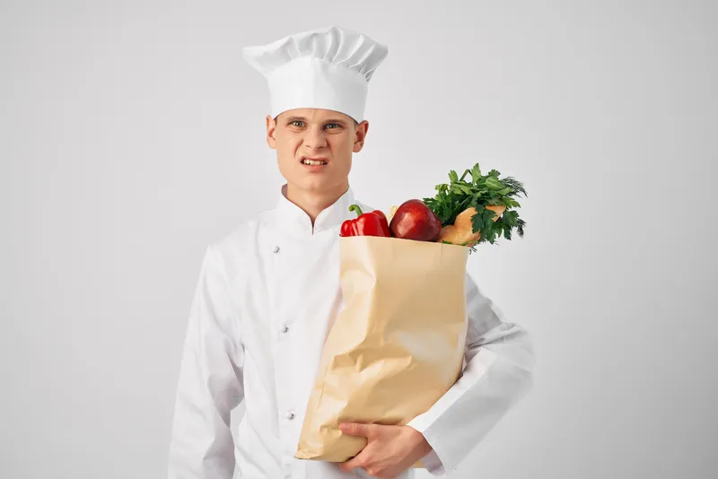 Шеф-повар с пакетом продуктов на кухне занимается приготовлением еды и работой