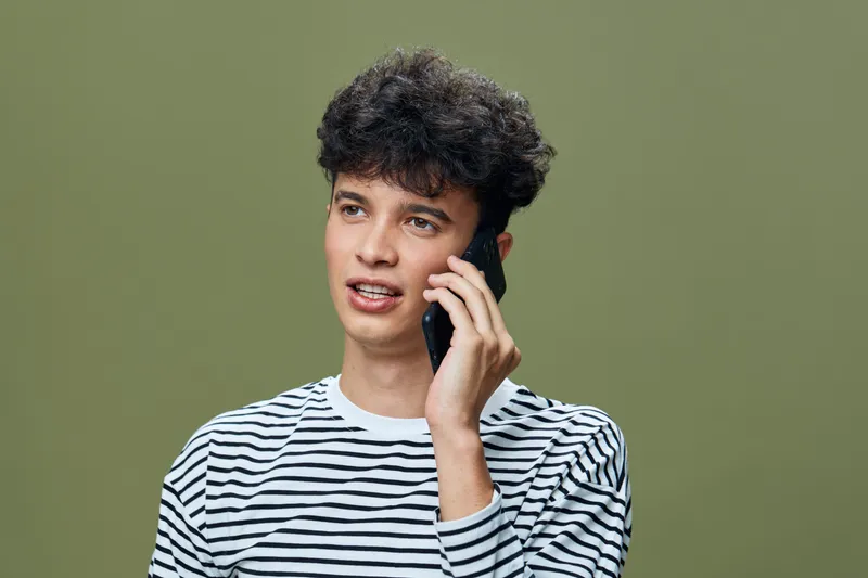 young man talking on phone, striped shirt, casual style, green background, communication, technology, indoors