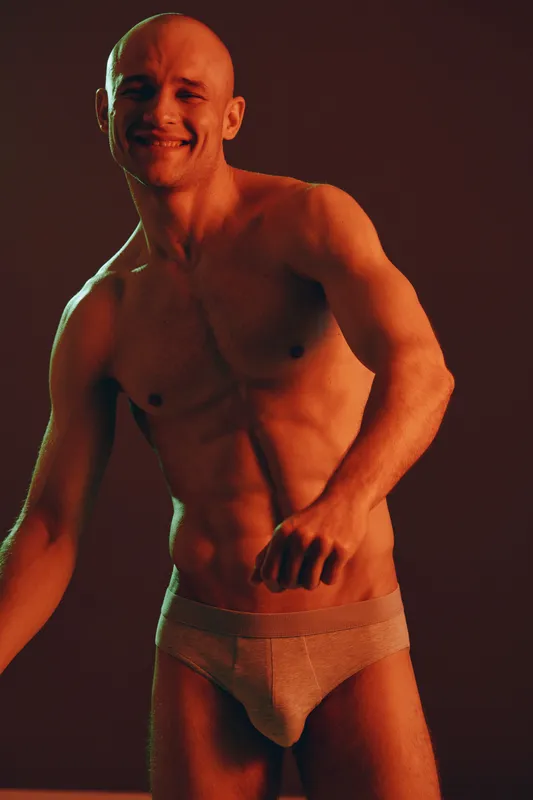 Smiling man in expressive lighting, showcasing a fit body and a confident pose. The playful atmosphere enhances the overall energy of the image, creating a vibrant feel.
