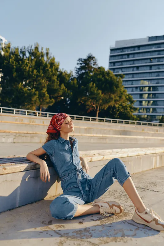 Lifestyle woman in modern boho-western denim street style sits relaxed outdoors with film color effect, casual and trendy outfit reflecting youthful urban vibe.
