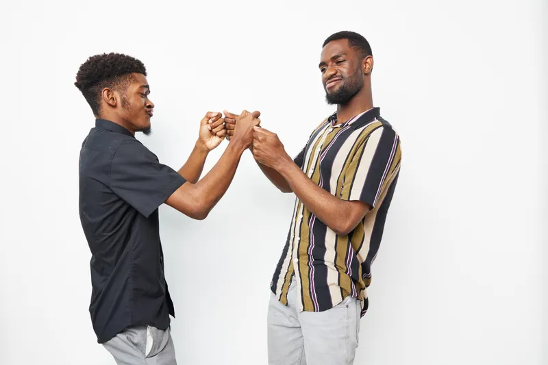 Two young Black men playfully fist bumping each other, showcasing friendship and camaraderie. Their cheerful expressions reflect a lighthearted moment together.