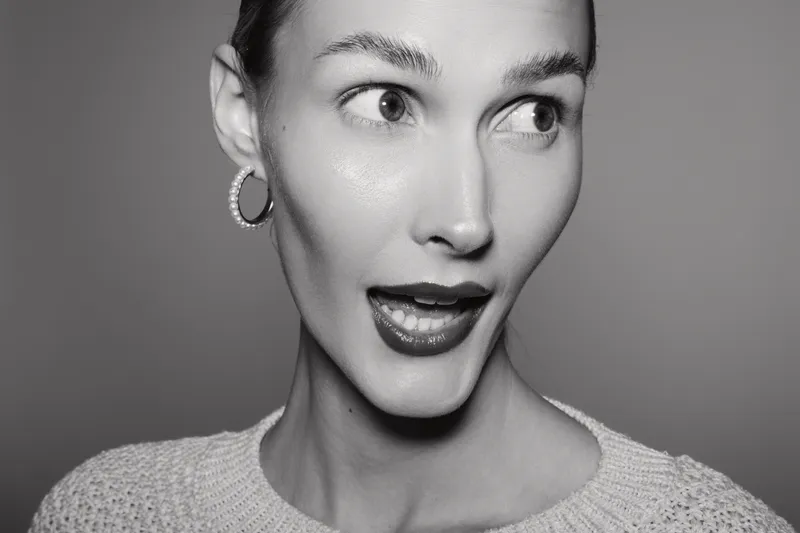 Surprised Caucasian woman with fair skin and short hair wears knitted sweater and hoop earrings in studio. Concept for emotions, expression, and portrait photography.