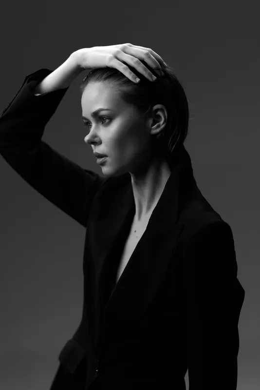 Black and white portrait of a thoughtful woman in a dark blazer with serious expression and hand on head.