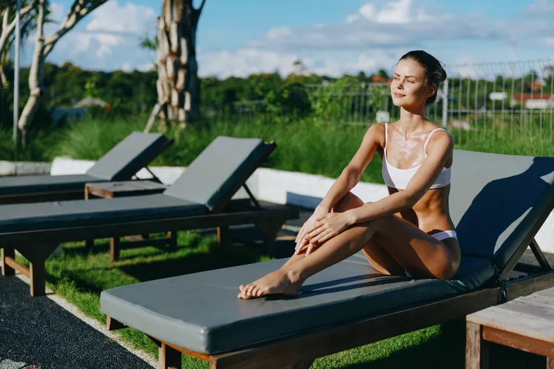 Woman lounge poolside outdoor summer relaxation sunshine bikini lifestyle leisure, she rests on a lounge chair by the pool under bright daylight in a calm outdoor setting