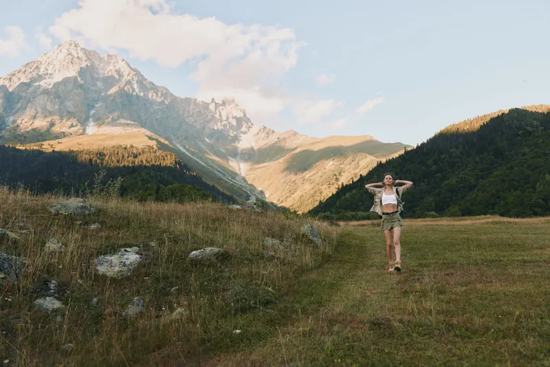 Young woman enjoying outdoor lifestyle runs through a mountain meadow, expressing health and vitality amid alpine scenery, bright daylight, and expansive hills.
