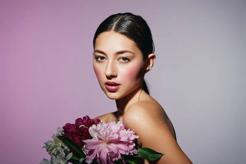 Молодая брюнетка с макияжем, цветком и румянами на лице, позирующая крупным планом на белом фоне