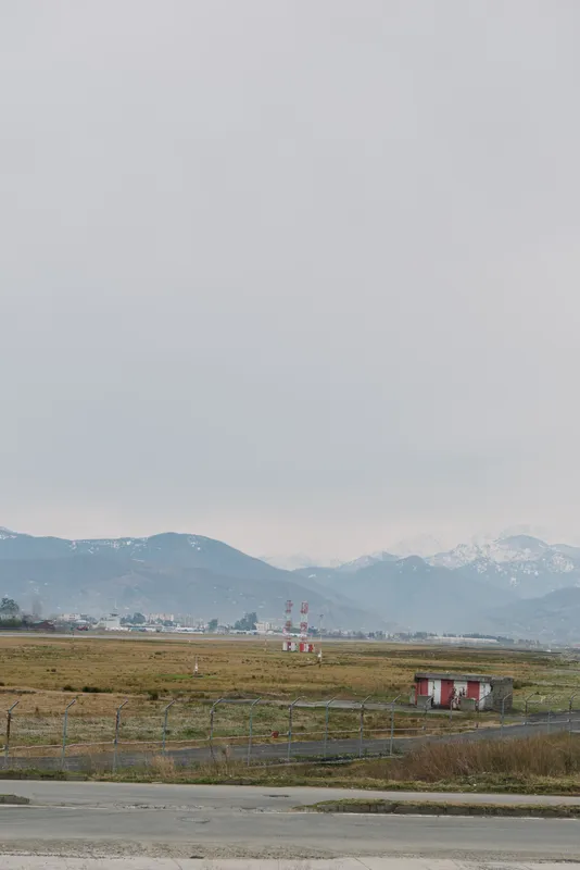 Rural landscape with open field, small building, and distant mountains under cloudy sky. Concept of nature, countryside, and peaceful environment in a remote area.