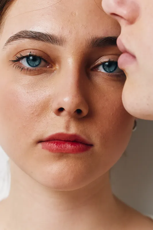 Women closeup portrait with natural skin and blue eyes facing camera while another woman with soft focus is near. Beauty, makeup, lips and intimate moment with tenderness.
