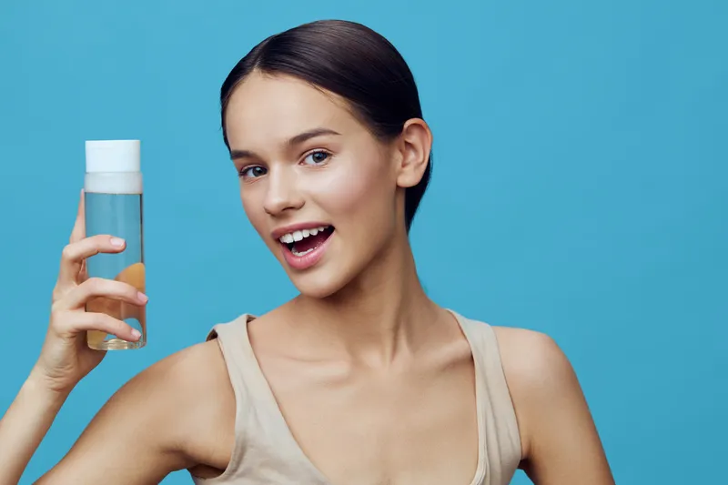 Young woman holding a refreshing drink, smiling with confidence against a vibrant blue background, embodying a healthy lifestyle and wellness