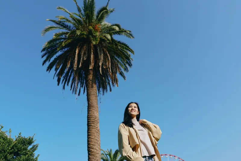 Palm, tree, woman, outdoor scene under a clear sky with sunshine showcasing casual fashion and travel vibes in a sunny park setting bright relaxed mood