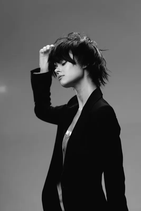 Black and white portrait of a young woman with short hair in a blazer, expressing calmness and style in a minimalist studio setting.