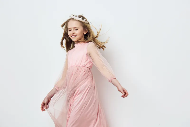 Happy girl in a pink dress dancing with joy, showcasing elegance and playfulness against a light background Perfect for children s fashion or celebration concepts