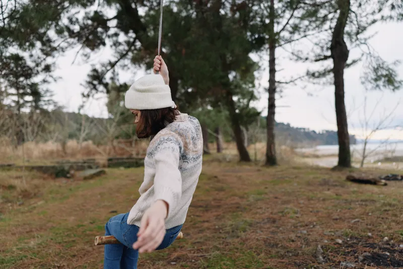 Outdoor swing, woman in casual sweater and beanie, nature and forest setting, swinging motion, relaxed park moment on a wooden swing in a tranquil outdoor scene