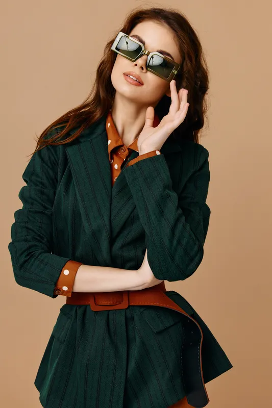 Симпатичная брюнетка в солнцезащитных очках и костюме, мода, гламур, бежевый фон