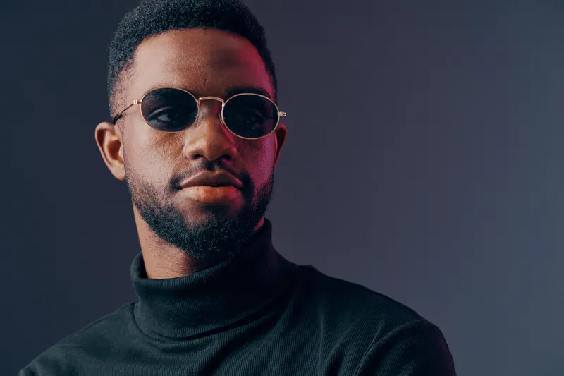 Stylish African man wearing sunglasses and a turtleneck, showcasing confidence against a dark gradient background, perfect for fashion and lifestyle concepts