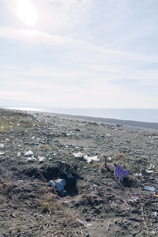 A beach with scattered litter along a rocky shoreline and a calm sea under a bright sky, highlighting coastal pollution and waste.