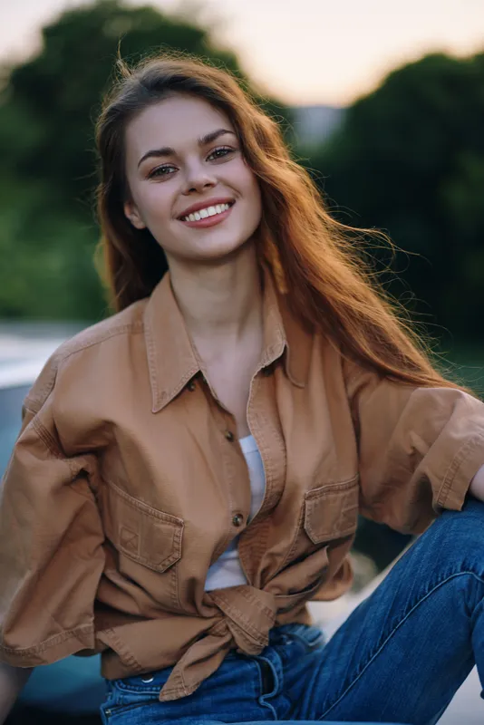 Young woman with long hair, smiling in a casual outfit, showcasing summer vibes and natural beauty against a blurred green background.
