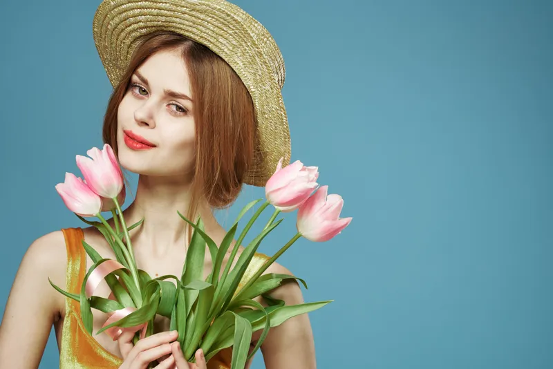 Жизнерадостная женщина в шляпе с букетом цветов, элегантность и роскошь в студии, кадр обрезан