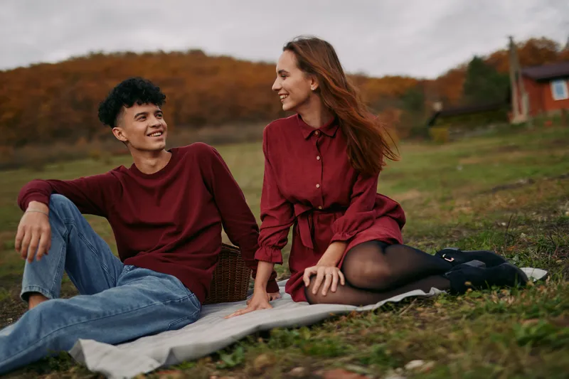 A genuine candid portrait of a young couple sharing a relaxed outdoor moment on a meadow blanket, conveying authentic emotion and accurate interpersonal connection in soft autumn light.