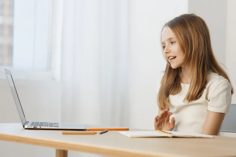 Happy young girl communicating online while working from home, showcasing a playful and engaged expression in a bright, minimalistic setting