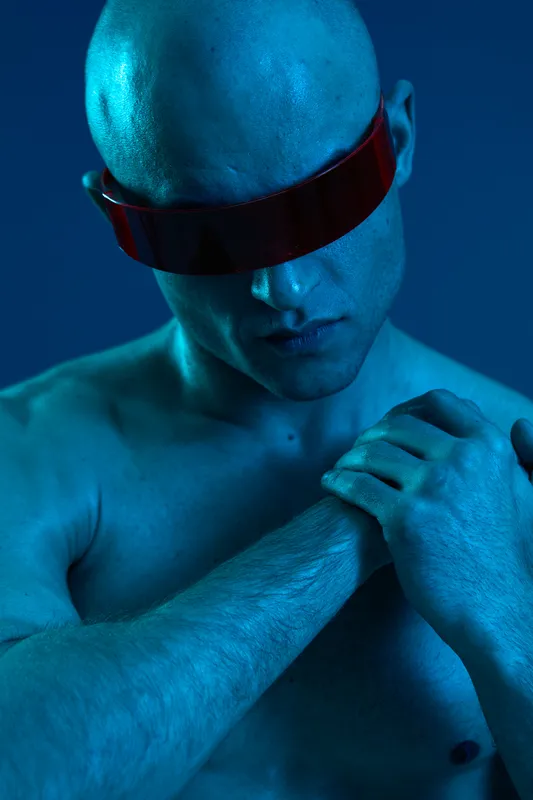 A muscular man with futuristic sunglasses, showcasing unique blue lighting and an artistic touch. An intriguing black and white photographic concept.