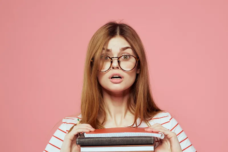 Молодая студентка с книгами на розовом фоне, в очках