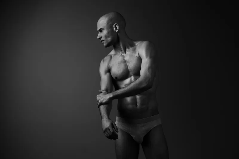 Black and white image of a muscular man showcasing strength and confidence, emphasizing his physique and male form in a striking visual composition.