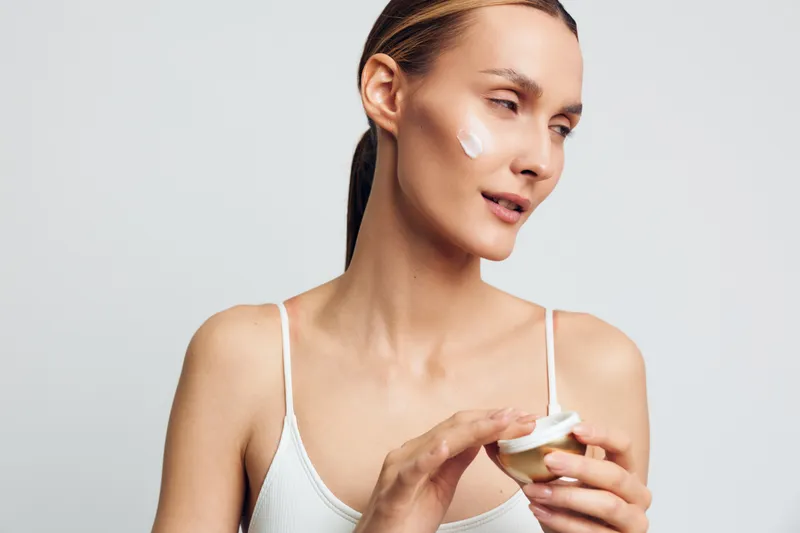 woman skincare beauty cream jar close up studio white background young female portrait holding moisturizer container, calm thoughtful expression, soft light, minimal clean setup, focus on hands and