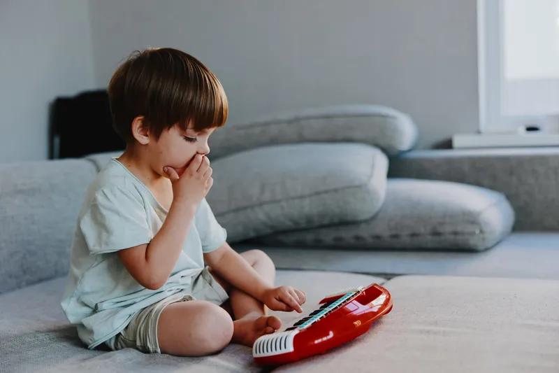 Curious boy playing with a toy keyboard, exploring sounds and music, enjoying a moment of creativity and imagination while seated on a comfortable couch.