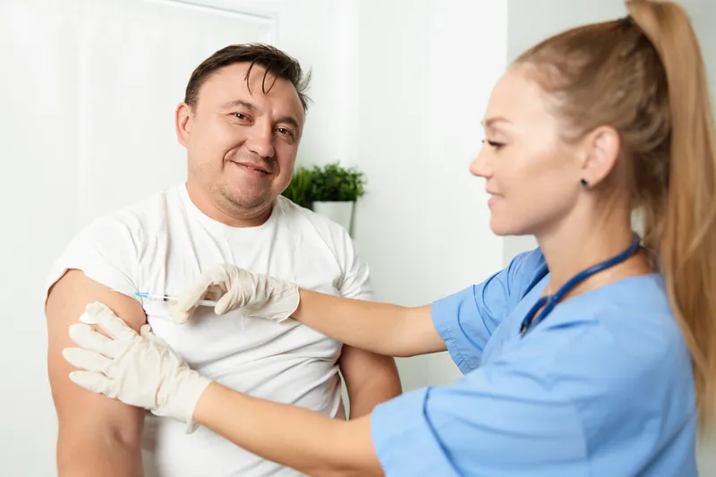 Женщина-врач делает инъекцию в руку мужчине в условиях больницы