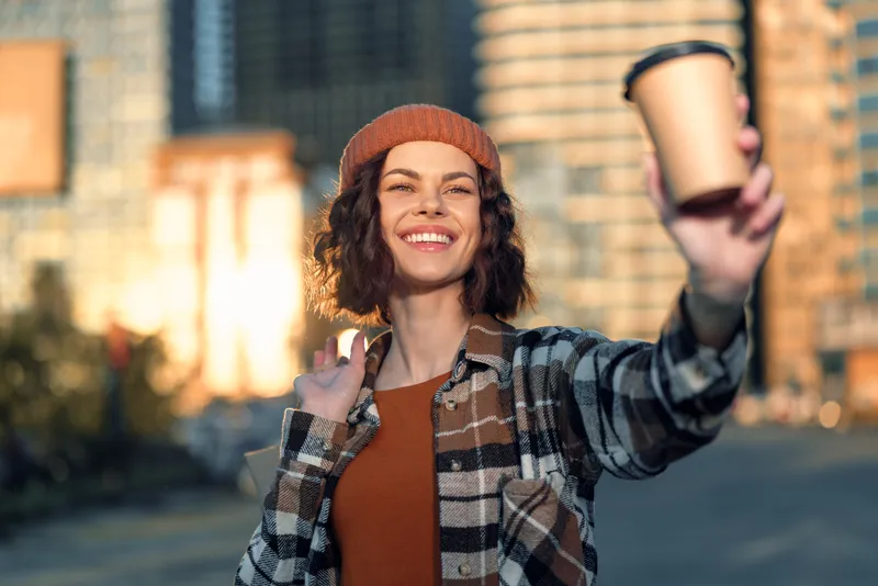 woman coffee smile urban candid beanie sunlight takeaway. Portrait of a young woman holding a takeaway cup at golden hour glow, authenticity and mindful living with emotional storytelling, casual