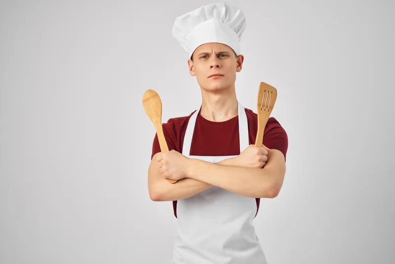 Повар-мужчина в белом фартуке с кухонной утварью готовит в ресторане