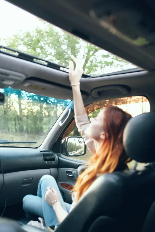 Женщина с открытым окном на переднем сиденье автомобиля жестикулирует руками, интерьер салона, попутчица