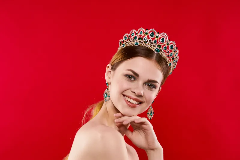 Фотография высокого качества: жизнерадостная женщина с обнажёнными плечами, украшениями и короной, излучающая очарование
