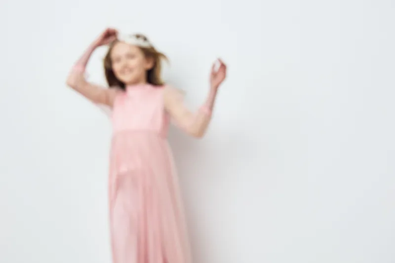Happy girl in a pink dress dancing against a light background, embodying joy and innocence, perfect for seasonal themes and children s fashion