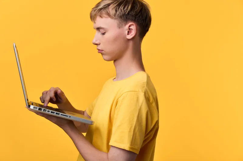 Young man in a yellow shirt works on a laptop against a bright yellow background, concentration on the screen, exploring technology, learning process, digital activity, modern study scene, energetic
